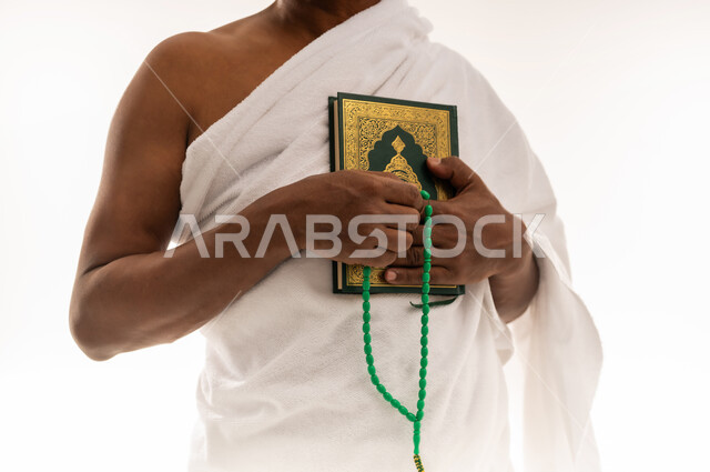 قراءة الأذكار والأدعية، حفظ وتلاوة القرآن الكريم، بورتريه مقرب لرجل عربي سعودي خليجي يرتدي لباس الإحرام يحمل بيده السبحة والمصحف الشريف، مفهوم العبادة والتقرب إلى الله تعالى ، سيد عماني يقوم باداء مناسك الحج والعمرة، خلفية بيضاء