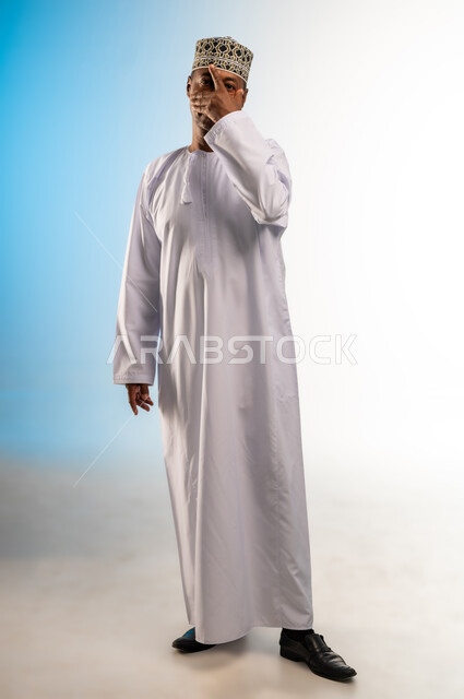 الشعور بالخجل والإحراج، محاولة استراق النظر، البكاء ومشاعر الحزن، إغماض العينين وعدم الرغبة بالرؤية، التعرض لصدمة وعدم التصديق، بورتريه لرجل عربي خليجي عماني يرتدي الدشداشة والكمة يغطي وجهه بيده، الجسم بالطول الكامل، خلفية ملونة
