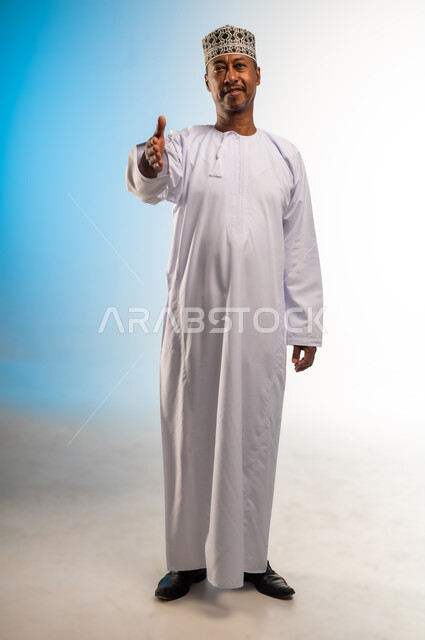 إلقاء التحيه والسلام, مفهوم الاستقبال والترحيب, التعارف و الصداقه وتكوين علاقات, بورتريه لرجل عربي خليجي عماني مبتسم يرتدي الدشداشة و الكمه ينظر الى الكاميرا يمد كفه للمصافحة بإيماءات السرور والبشاشة، خلفية ملونة