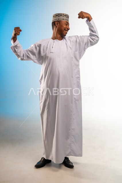 Healthy diet, fitness, exercise, building muscle mass, concept of strength and masculinity, portrait of a smiling Omani Gulf Arab man wearing a dishdasha and a thobe looking at his muscles with gestures of happiness, full body, colorful background
