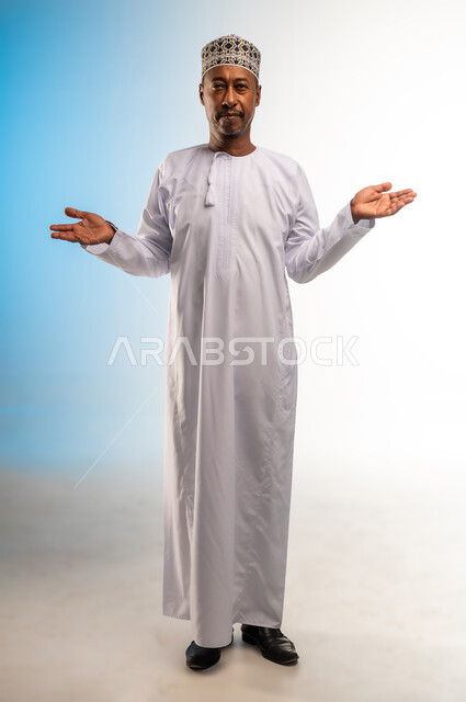 النظر الى الكاميرا بتعابير التردد وعدم الثقة بخصوص أمر معين، بورتريه لرجل عربي خليجي عماني يرتدي الدشداشة و الكمه يرفع كفيه للاعلى بإيماءات عدم التأكد، الشعور بالحيرة وعدم المعرفة، صورة الجسم بالطول الكامل, خلفية بيضاء