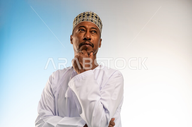 Trying to solve problems and make decisions, contemplating and concentrating to find a solution to a problem, feeling bored and upset, close-up portrait of an Arab Gulf Omani man wearing a dishdasha and a sleeve, putting his hand on his face with gestures of thinking, confusion and annoyance, colorful background