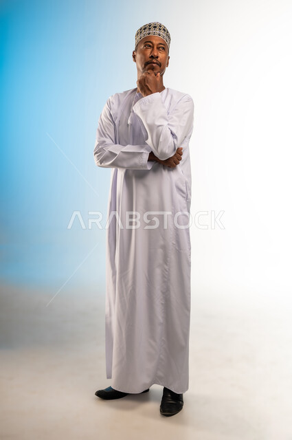 التمعن والتركيز لإيجاد الحل لمشكلة ما, الشعور بالضيق والملل، حل المشكلات واتخاذ القرارات، بورتريه لرجل عربي خليجي عماني يرتدي الدشداشة و الكمه يضع يده على وجهه بإيماءات التفكير والحيرة والانزعاج، صورة الجسم بالطول الكامل, خلفية ملونة