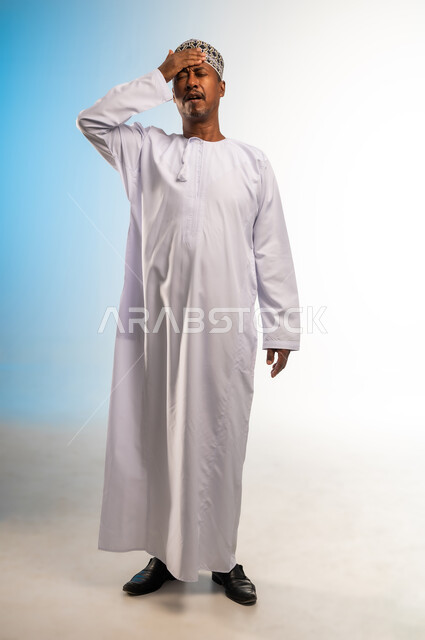 الاحساس بالشقيقية والصداع النصفي, الشعور بالإرهاق وفقدان التركيز, الاجهاد والضغط النفسي, بورتريه لرجل عربي خليجي عماني يرتدي الدشداشة و الكمه يضع يديه على رأسه ويغمض عينيه بإيماءات ألم الرأس الشديد, صورة الجسم بالطول الكامل, خلفية ملونة