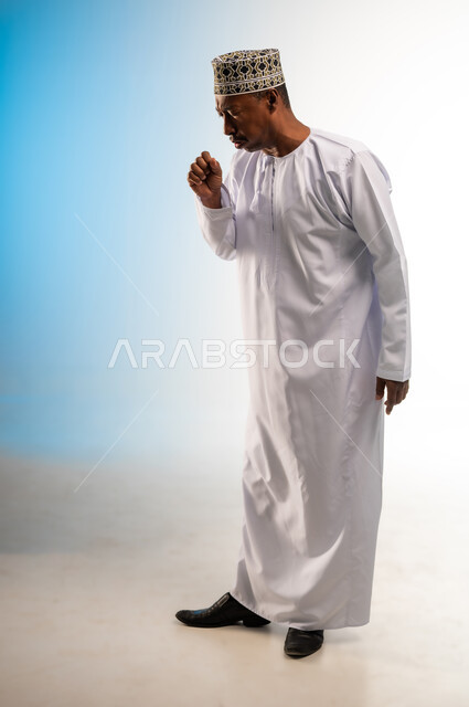 الاصابة بنزلة برد، أعراض فايروس كورونا (كوفيد-19),  الحاجة لطلب المساعدة و الذهاب الى الطبيب, بورتريه لرجل عربي خليجي عماني يرتدي الدشداشة و الكمه يضع يده على فمه بإيماءات السعال و الألم, الشعور بالمرض و التعب والإرهاق, صورة الجسم بالطول الكامل، خلفية ملونة
