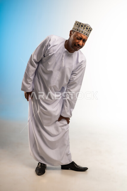 الإحساس بألم في الركبة والمفاصل، الانزعاج والصعوبة بالمشي، آلام شديدة صعبة التحمل، بورتريه لرجل عربي خليجي عماني يرتدي الدشداشة و الكمه يضع يده على ركبته بتعابير التعب، صورة الجسم بالطول الكامل، خلفية ملونة