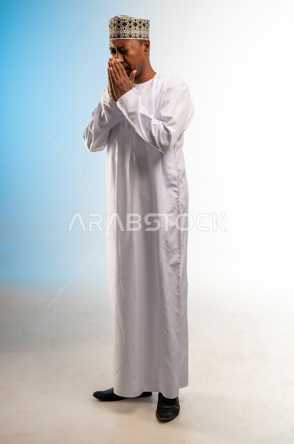 الشعور بالتعب الشديد، تعابير المرض والإرهاق، الإصابة بالزكام والانفلونزا، بورتريه لرجل عربي عماني خليجي يرتدي الكمه و الدشداشة يرفع كفيه عاليا بايماءات العطاس, صورة الجسم بالطول الكامل ,خلفية ملونة