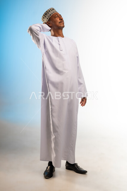 الحاجه للعلاج و طلب المساعده, الإحساس بالدوار والتعب والإرهاق, بورتريه لرجل عربي عماني خليجي يرتدي الكمه و الدشداشة يضع يده على رأسه بإيماءات الوجع, الشعور بالصداع و ألم بالرأس, صورة الجسم بالطول الكامل، خلفية ملونة