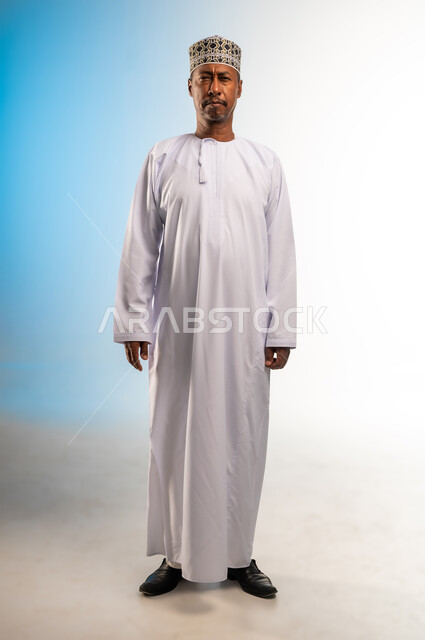 المعاناة من ضعف النظر, اغماض العينين قليلا بايماءات محاولة الرؤية، بورتريه  لرجل عربي عماني خليجي يرتدي الكمه و الدشداشة يقف باستقامة و ينظر الى الكاميرا, صورة الجسم بالطول الكامل, خلفيه ملونة
