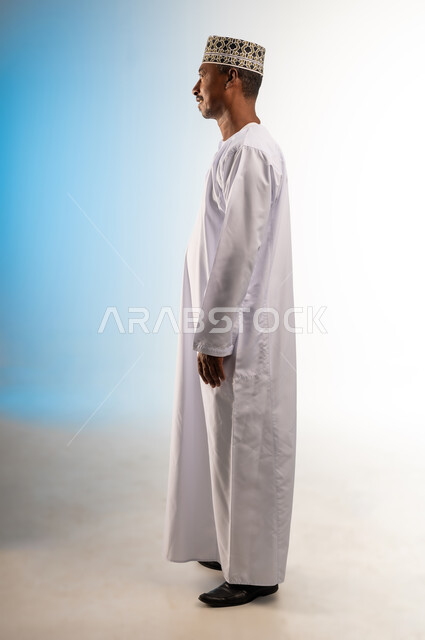 Concern for elegance and appearance, concept of masculinity and self-confidence, taking personal photos for official documents, side portrait of a smiling Arab Gulf Omani man wearing a dishdasha and a turban standing straight looking at something, full-length body image, colored background