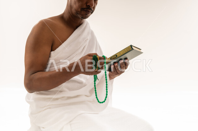 مفهوم العبادة و التقرب الى الله, رجل سعودي يقراءة المصحف الشريف، بورتريه لحاج عربي عماني خليجي يرتدي لباس الاحرام يحمل بيده السبحة و القرآن الكريم يقوم بتقبيله، اداء مناسك الحج والعمرة، خلفية بيضاء