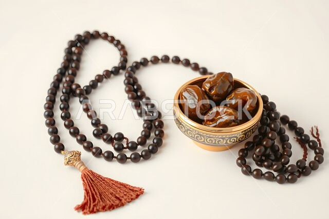 منتج ومحصول محلي وطني، وجبة غذائية بسعرات حراريه مفيدة، افطار الصائم في رمضان، غذاء صحي ومفيد، الالتزام والتمسك بالأذكار، ضيافة المناسبات والأعياد في المملكة العربية السعودية، وعاء مليء بالتمر بجانب سبحه مصنوعه من الخرز لذكر الله تعالى