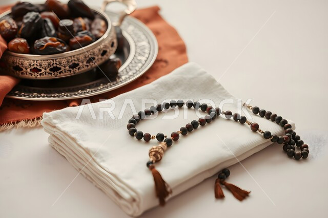 افطار الصائم في رمضان، منتج ومحصول محلي وطني، وجبة غذائية بسعرات حراريه مفيدة، غذاء صحي ومفيد، الالتزام والتمسك بالأذكار، ضيافة المناسبات والأعياد في المملكة العربية السعودية، وعاء مليء بالتمر بجانب سبحه مصنوعه من الخرز لذكر الله تعالى