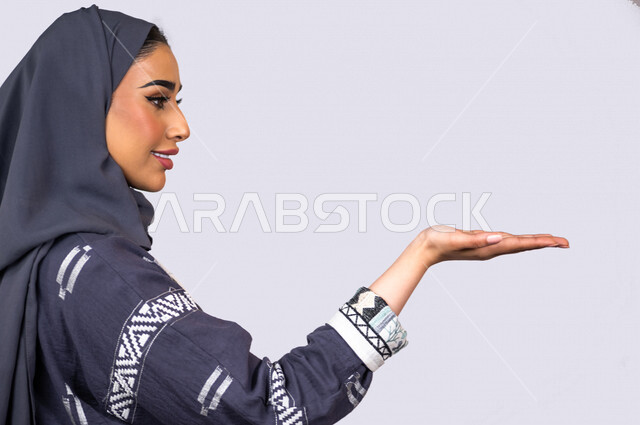 بورتريه لمرأة عربية خليجية سعودية ، تقوم بإيماءات يد مختلفة ، تحمل شيء ما ، رفع عنصر هولوجرامي ، شابة سعودية مسلمة محجبة ترتدي العباءة الخليجية ، خلفية بيضاء