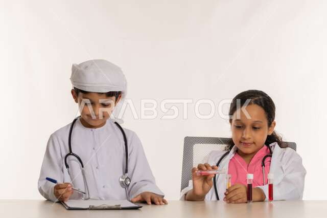 تحديد واختيار المهنة المستقبلية منذ الصغر، اجراء تجارب وتفاعلات حيويه في المختبر، بورتريه لفتاة عربية خليجية اماراتية ترتدي المعطف الأبيض وتستخدم انابيب الاختبار، ولد عربي خليجي اماراتي يرتدي الكندورة والعمامة يقوم بتدوين وكتابة النتائج،  خلفية بيضاء