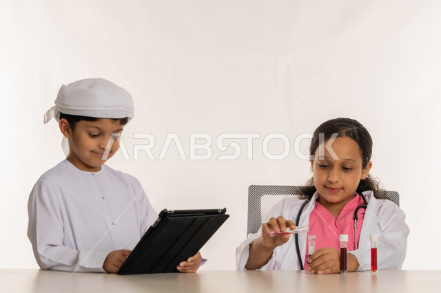 اجراء تجارب وتفاعلات حيويه في المختبر، بورتريه لفتاة عربية خليجية اماراتية ترتدي المعطف الأبيض وتستخدم انابيب الاختبار، ولد اماراتي يرتدي الكندورة والعمامة يمسك بيده الجهاز اللوحي، اختيار وتحديد المهنة المستقبلية منذ الصغر، استخدام جهاز تقني حديث ومتطور، خلفية بيضاء