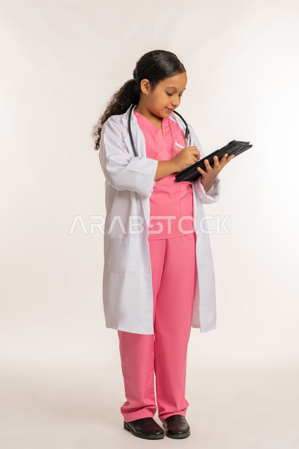 استخدام قلم التابليت لتدوين الملاحظات، الطموح والهدف المستقبلي بالعمل في العيادات والمشافي، كتابة نتائج الفحوصات، بورتريه لفتاة عربية خليجية اماراتية ترتدي معطف أبيض تحمل بيدها الجهاز اللوحي، بنت سعودية  تقوم بإعداد التقارير الطبيه، صورة لكامل الجسم، خلفية بيضاء