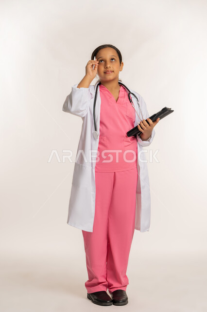 كتابة نتائج الفحوصات، استخدام قلم التابليت لتدوين الملاحظات، بورتريه لفتاة عربية خليجية اماراتية ترتدي معطف أبيض تحمل بيدها الجهاز اللوحي، بنت سعودية تقف بايماءات التفكير تقوم بإعداد التقارير الطبيه، صورة لكامل الجسم، خلفية بيضاء