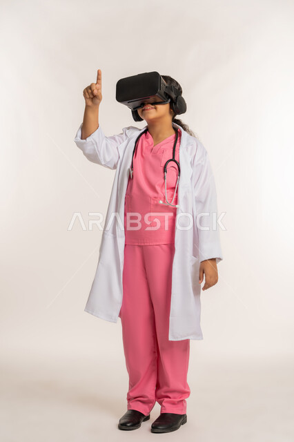 تحديد موقع شيء معين، دمج  الطب والرعاية الصحية مع الواقع الافتراضي، بورتريه لفتاة عربية خليجية اماراتية ترتدي المعطف الأبيض تضع نظارة الفي ار تقوم بالتفاعل مع العالم الخيالي، بنت سعودية تشير باصبع السبابة إلى مكان ما، صورة لكامل الجسم، خلفية بيضاء