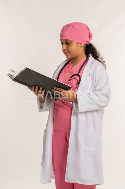 الأهداف والطموحات المستقبلية، الاجتهاد للوصول إلى الغايات، مفهوم الطب والرعاية الصحية، بورتريه لفتاة عربية خليجية اماراتية ترتدي المعطف الأبيض تضع السماعة الطبية تحمل بيدها كتاب، صبية سعودية تقوم بالقراءة بايماءات التركيز، خلفية بيضاء