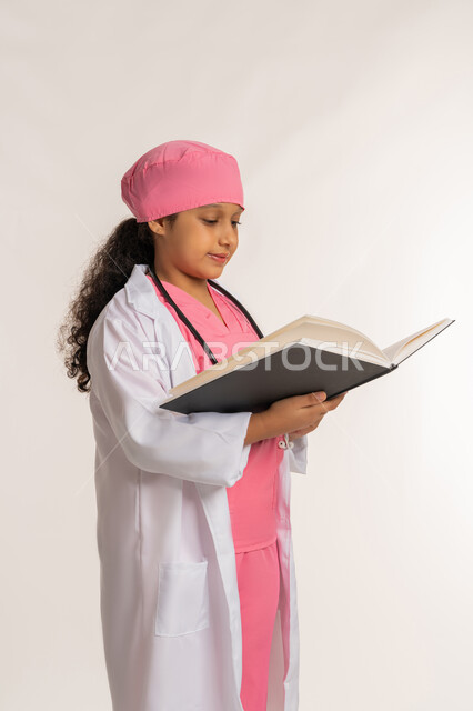 بنت سعودية تقوم بالقراءة بايماءات التركيز، مفهوم الطب والرعاية الصحية، الاجتهاد للوصول الى الطموح والهدف المستقبلي، بورتريه لفتاة عربية خليجية اماراتية ترتدي المعطف الأبيض تضع السماعة الطبية تحمل بيدها كتاب، خلفية بيضاء