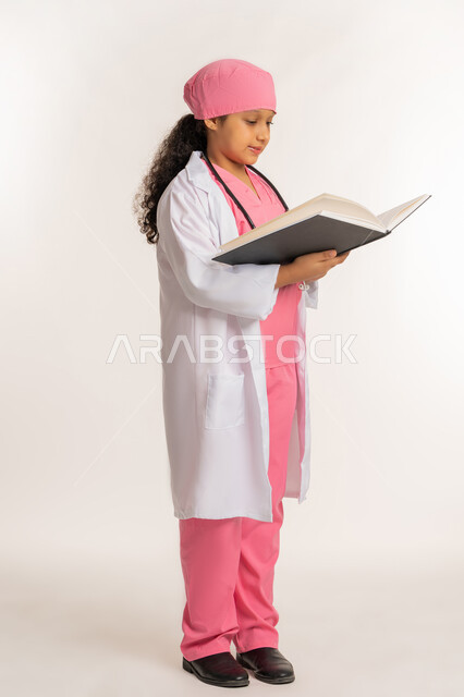 مفهوم الطب والرعاية الصحية، الاجتهاد للوصول الى الطموح والهدف المستقبلي، بورتريه من الجانب لفتاة عربية خليجية اماراتية ترتدي المعطف الأبيض تضع السماعة الطبية تحمل بيدها كتاب، بنت سعودية تقوم بالقراءة بايماءات التركيز، خلفية بيضاء