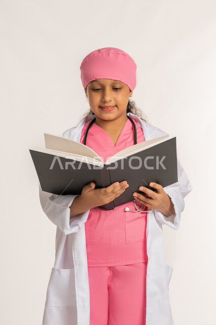 الاجتهاد للوصول الى الطموح والهدف المستقبلي، مفهوم الطب والرعاية الصحية، بورتريه لفتاة عربية خليجية اماراتية ترتدي المعطف الأبيض تضع السماعة الطبية تحمل بيدها كتاب، بنت سعودية تقوم بالقراءة بايماءات التركيز، خلفية بيضاء