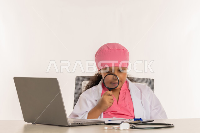 توضيح وتحسين رؤية، أدوات بصرية للتدقيق والتركيز، مفهوم الطب والرعاية الصحية، استخدام الاجهزة التقنية، بورتريه مقرب لبنت عربية خليجية اماراتية ترتدي المعطف الأبيض تجلس خلف المكتب تقوم بمراجعة سجل المرضى، فتاة سعودية تحمل بيدها عدسة مكبرة، خلفية بيضاء