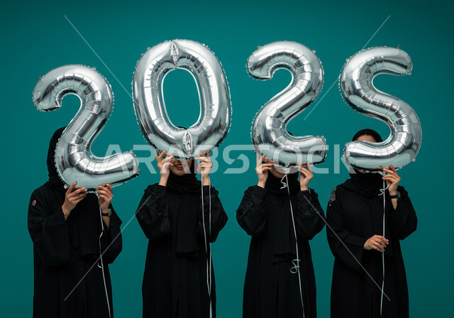 إيماءات السعادة والسرور, التفاؤل والترحيب بالسنة الجديدة, البهجة بقدوم العام الجديد, الاحتفال بعيد رأس السنة الميلادية 2025, بورتريه لنساء عربيات خليجيات سعوديات محجبات ترتدين العباءات السوداء تحملن بأيديهن بالونات فضية كبيرة, خلفية زرقاء