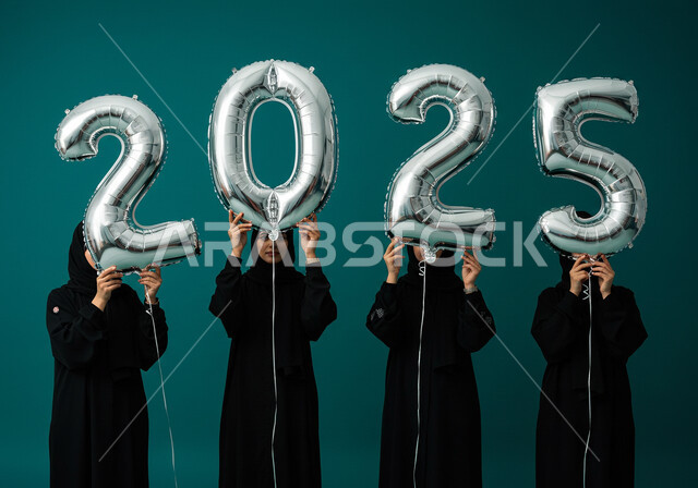 البهجة بقدوم العام الجديد, إيماءات السعادة والسرور, التفاؤل والترحيب بالسنة الجديدة, الاحتفال بعيد رأس السنة الميلادية 2025, بورتريه لنساء عربيات خليجيات سعوديات محجبات ترتدين العباءات السوداء تحملن بأيديهن بالونات فضية كبيرة, خلفية زرقاء