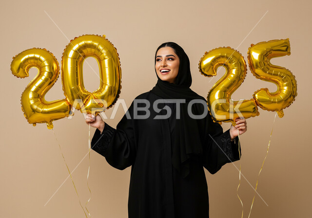 Joy of the New Year, gestures of happiness and joy, optimism and welcoming the New Year, celebrating New Year's Day 2025, portrait of a smiling veiled Saudi Arabian Gulf woman wearing a black abaya holding large golden balloons in her hand, beige background