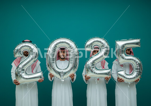الاحتفال بعيد رأس السنة الميلادية 2025, البهجة بقدوم العام الجديد, إيماءات السعادة والسرور, التفاؤل والترحيب بالسنة الجديدة, بورتريه لرجال عرب خليجيين سعوديين يرتدون الثوب التقليدي والشماغ يحملون بأيديهم بالونات فضية كبيرة, خلفية زرقاء