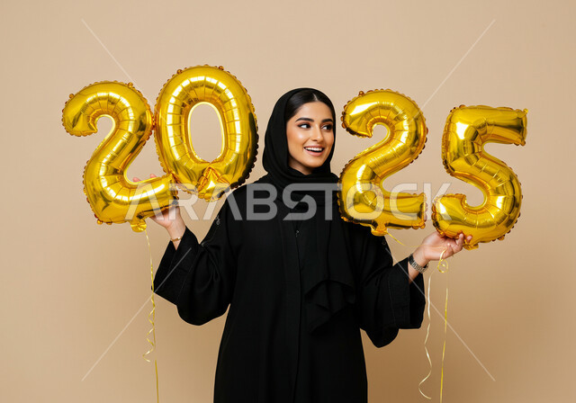 تعابير الفرح والسعادة والسرور, البهجة والتفاؤل والترحيب بالسنة الجديدة, الاحتفال بعيد رأس السنة الميلادية 2025, بورتريه لامرأة عربية خليجية سعودية مبتسمة محجبة ترتدي العباءة السوداء تحمل بيدها بالونات ذهبية كبيرة, الاستعداد لاستقبال العام الجديد, خلفية بيج