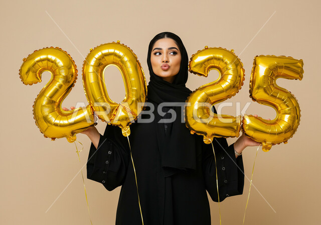 الاستعداد لاستقبال العام الجديد, الاحتفال بعيد رأس السنة الميلادية 2025, تعابير الفرح والسعادة والسرور, البهجة والتفاؤل والترحيب بالسنة الجديدة, بورتريه لامرأة عربية خليجية سعودية محجبة ترتدي العباءة السوداء تحمل بيدها بالونات ذهبية كبيرة, خلفية بيج