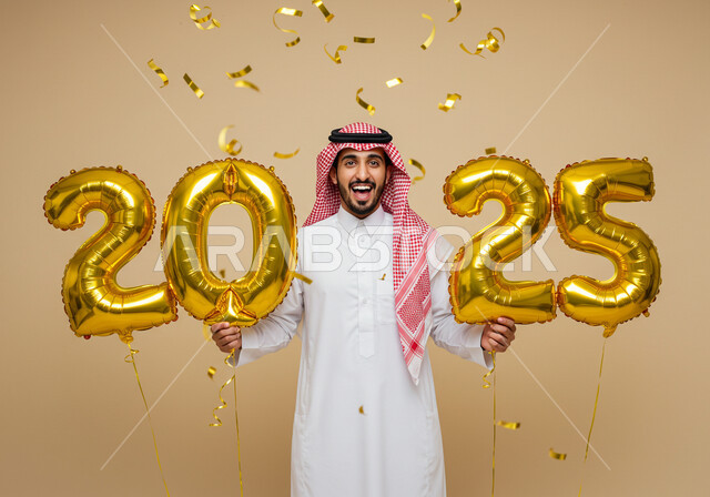 التفاؤل والترحيب بالسنة الجديدة, إيماءات السعادة والسرور, الاستعداد لاستقبال العام الجديد, بورتريه لرجل عربي خليجي سعودي مبتسم يرتدي الثوب التقليدي والشماغ يحمل بيديه بالونات ذهبية كبيرة, الاحتفال بعيد رأس السنة الميلادية 2025, خلفية بيج