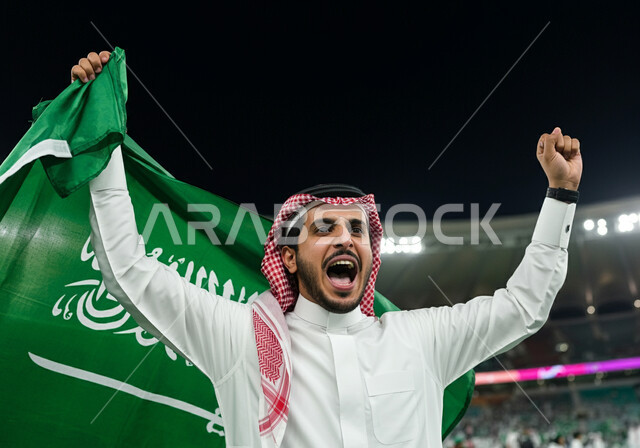 الاحتفال بالأعياد والمناسبات الوطنية, اليوم الوطني السعودي 23 سبتمبر, ذكرى يوم العلم 11 مارس، رجل عربي خليجي سعودي يرتدي الثوب التقليدي والشماغ يحمل علم المملكة ويقف في الملعب، تشجيع المنتخب السعودي،  الاهتمام بالرياضة والانشطة الترفيهية، ايماءات الحماس والسرور