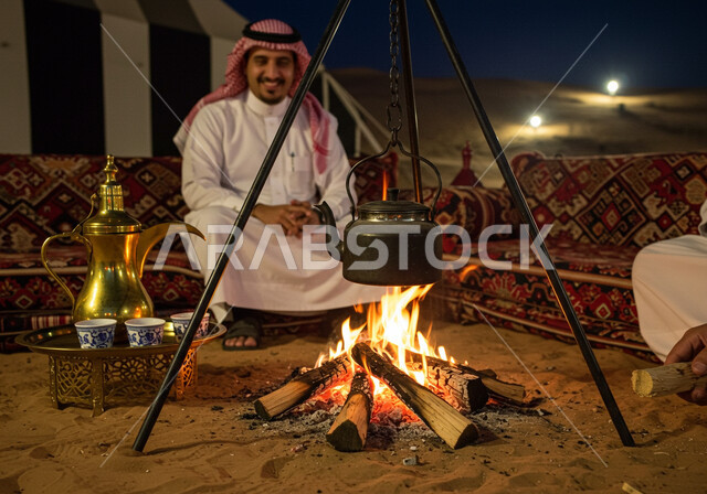 رحلة تخييم سياحية ممتعة وسط الصحراء، الجو الليلي الهادئ, رجل عربي خليجي سعودي يرتدي الثوب التقليدي والشماغ يجلس أمام شعلة الحطب، مخيم سياحي في منطقة صحراوية، كشتة و جلسة بر شبابية, التشكيلات والكثبان الرملية, الرمال الذهبية الناعمة