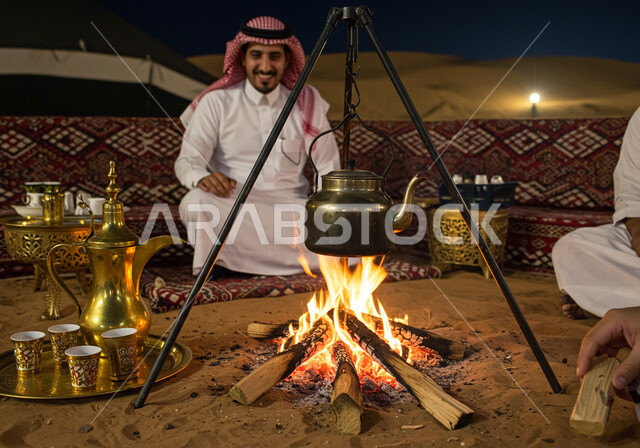 الجو الليلي الهادئ, رجل عربي خليجي سعودي يرتدي الثوب التقليدي والشماغ يجلس أمام شعلة الحطب، مخيم سياحي في منطقة صحراوية، كشتة و جلسة بر شبابية, التشكيلات والكثبان الرملية, الرمال الذهبية الناعمة، رحلة تخييم سياحية ممتعة وسط الصحراء