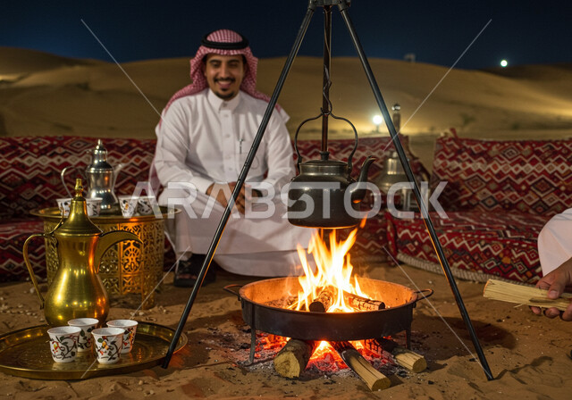  كشتة و جلسة بر شبابية, التشكيلات والكثبان الرملية, الرمال الذهبية الناعمة, رحلة تخييم سياحية ممتعة وسط الصحراء، الجو الليلي الهادئ, رجل عربي خليجي سعودي يرتدي الثوب التقليدي والشماغ يجلس أمام شعلة الحطب، مخيم سياحي في منطقة صحراوية