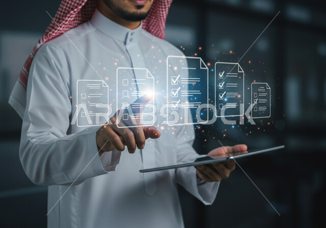 رؤية مستقبلية سعودية 2030 ، دمج التقنيات الحديثة في العمل، استخدام جهاز تقني حديث ومتطور، صورة مقربة لرجل عربي خليجي سعودي يرتدي الثوب التقليدي والشماغ يمسك بيده الايباد يقوم بالنقر على أوراق مهام هولوجرامية