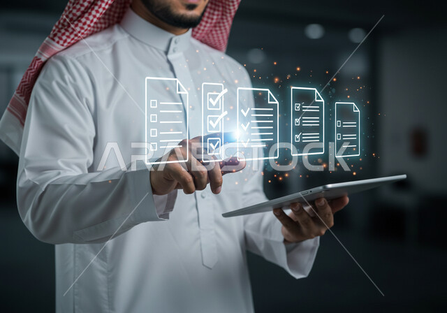 رؤية مستقبلية سعودية 2030 ، دمج التقنيات الحديثة في العمل، استخدام جهاز تقني حديث ومتطور، صورة مقربة لرجل عربي خليجي سعودي يرتدي الثوب التقليدي والشماغ يمسك بيده الايباد يقوم بالنقر على أوراق مهام هولوجرامية