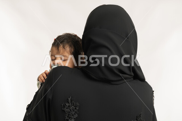 بناء علاقة متينة مع الأبناء، استمداد الرضيع الطمأنينة والاستقرار من الأم، بورتريه مقرب من الخلف لسيدة عربية خليجية إماراتية ترتدي الحجاب والعباءة تحمل طفلها بحنان، تلبية احتياجات الأطفال الجسدية والعاطفية، امرأة سعودية تقوم بقضاء وقت ممتع مع ابنها، خلفية بيضاء