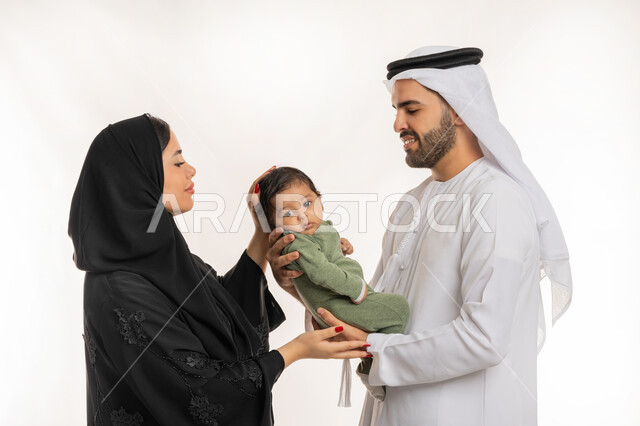 تحمل المسؤولية والعناية بالأطفال، قضاء وقت ممتع مع الطفل, بورتريه مقرب لعائلة عربية خليجية إماراتية مع ابنهم الرضيع, إيماءات الحب والحنان على الصغار, مفهوم الاسرة السعيدة, ملاعبة الأبناء بعطف واهتمام، خلفية بيضاء