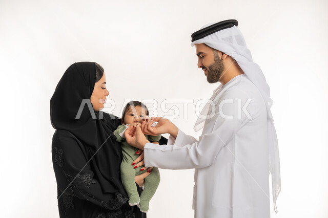 ملاعبة الأبناء بعطف واهتمام، مفهوم الاسرة السعيدة, قضاء وقت ممتع مع الطفل, بورتريه مقرب لعائلة عربية خليجية إماراتية مع ابنهم الرضيع, إيماءات الحب والحنان على الصغار, تحمل المسؤولية والعناية بالأطفال، خلفية بيضاء