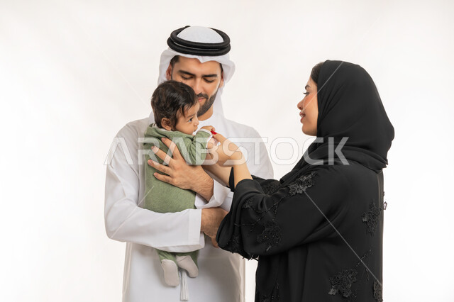 تحمل المسؤولية والعناية بالأطفال، قضاء وقت ممتع مع الطفل, بورتريه مقرب لعائلة عربية خليجية إماراتية مع ابنهم الرضيع, مفهوم الاسرة السعيدة, ملاعبة الأبناء بعطف واهتمام، إيماءات الحب والحنان على الصغار, خلفية بيضاء