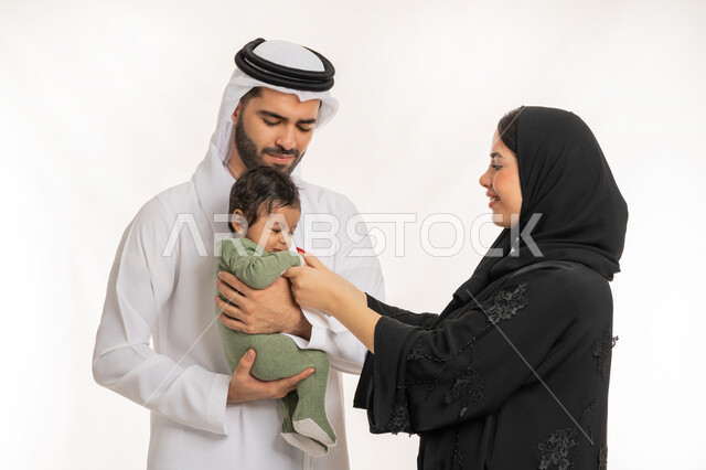 إيماءات الحب والحنان على الصغار, تحمل المسؤولية والعناية بالأطفال، قضاء وقت ممتع مع الطفل, بورتريه مقرب لعائلة عربية خليجية إماراتية مع ابنهم الرضيع, مفهوم الاسرة السعيدة, ملاعبة الأبناء بعطف واهتمام، خلفية بيضاء