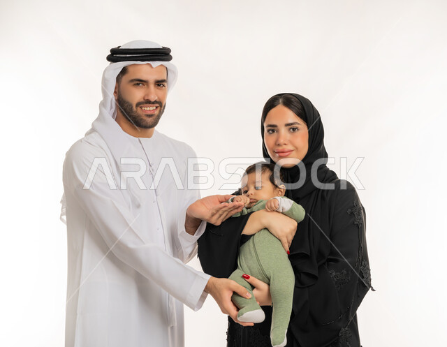 ملاعبة الأبناء بعطف واهتمام، مفهوم الاسرة السعيدة, قضاء وقت ممتع مع الطفل, بورتريه مقرب لعائلة عربية خليجية إماراتية مع ابنهم الرضيع, إيماءات الحب والحنان على الصغار, تحمل المسؤولية والعناية بالأطفال، خلفية بيضاء