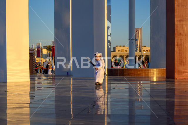 الفخر والاعتزاز بالهوية القطرية, مفهوم الحب والانتماء للبلاد, صورة من الخلف لولد عربي خليجي قطري يرتدي الثوب التقليدي والغترة البيضاء يمسك بيده سيف, الاحتفال بالأعياد والمناسبات الوطنية, اليوم الوطني لدولة قطر 18 ديسمبر