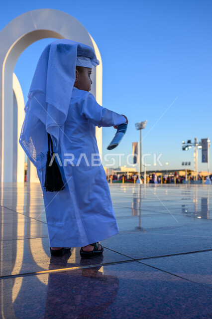 اليوم الوطني لدولة قطر 18 ديسمبر, الفخر والاعتزاز بالهوية القطرية, مفهوم الحب والانتماء للبلاد, صورة من الخلف لولد عربي خليجي قطري يرتدي الثوب التقليدي والغترة البيضاء يمسك بيده سيف, الاحتفال بالأعياد والمناسبات الوطنية