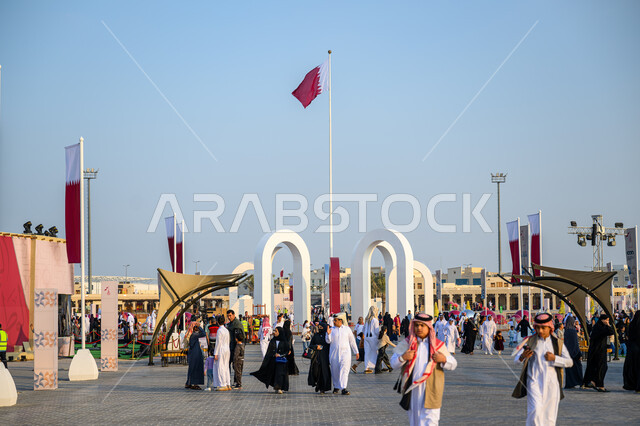 علم دولة قطر يرفرف في السماء, الأعياد والمناسبات الوطنية, الاحتفال باليوم الوطني القطري 18 ديسمبر, مفهوم الحب والانتماء للبلاد, مجموعة من الأشخاص عربيين خليجيين قطريين يتجولون في إحدى الساحات في الدوحة